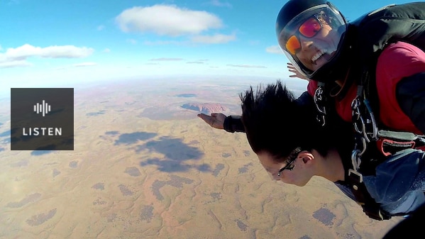 Image of Marley doing a tandem sky dive. Marley is looking at the camera grinning. They are very high in the sky. . Has Audio.