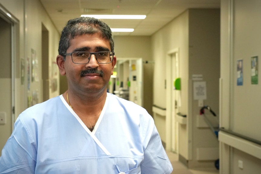 A man in blue hospital scrubs in the corridor of a hospital ward