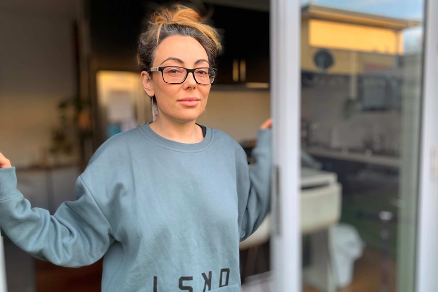 Sarah Goulding, wearing glasses and with her hair up, stands in the doorway of her home.