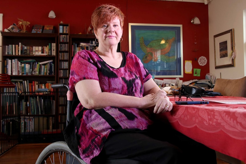 Ms Jenkins, in a wheelchair, in her living room with bookshelves behind her.