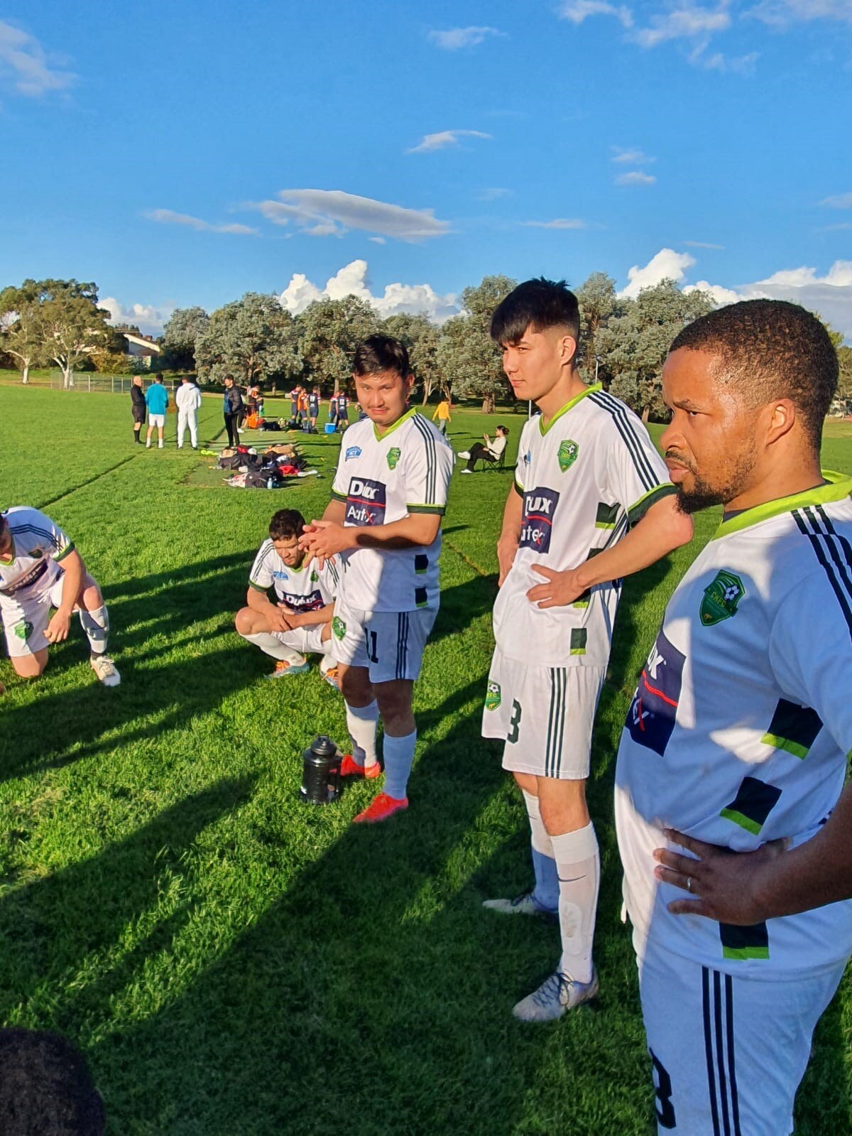 Men wearing football kits stand on the sideline of a football pitch.