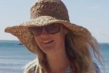 Samantha Fraser wears a large hat and sunglasses while walking along a beach.