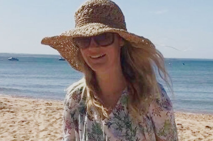 Samantha Fraser wears a large hat and sunglasses while walking on the beach.