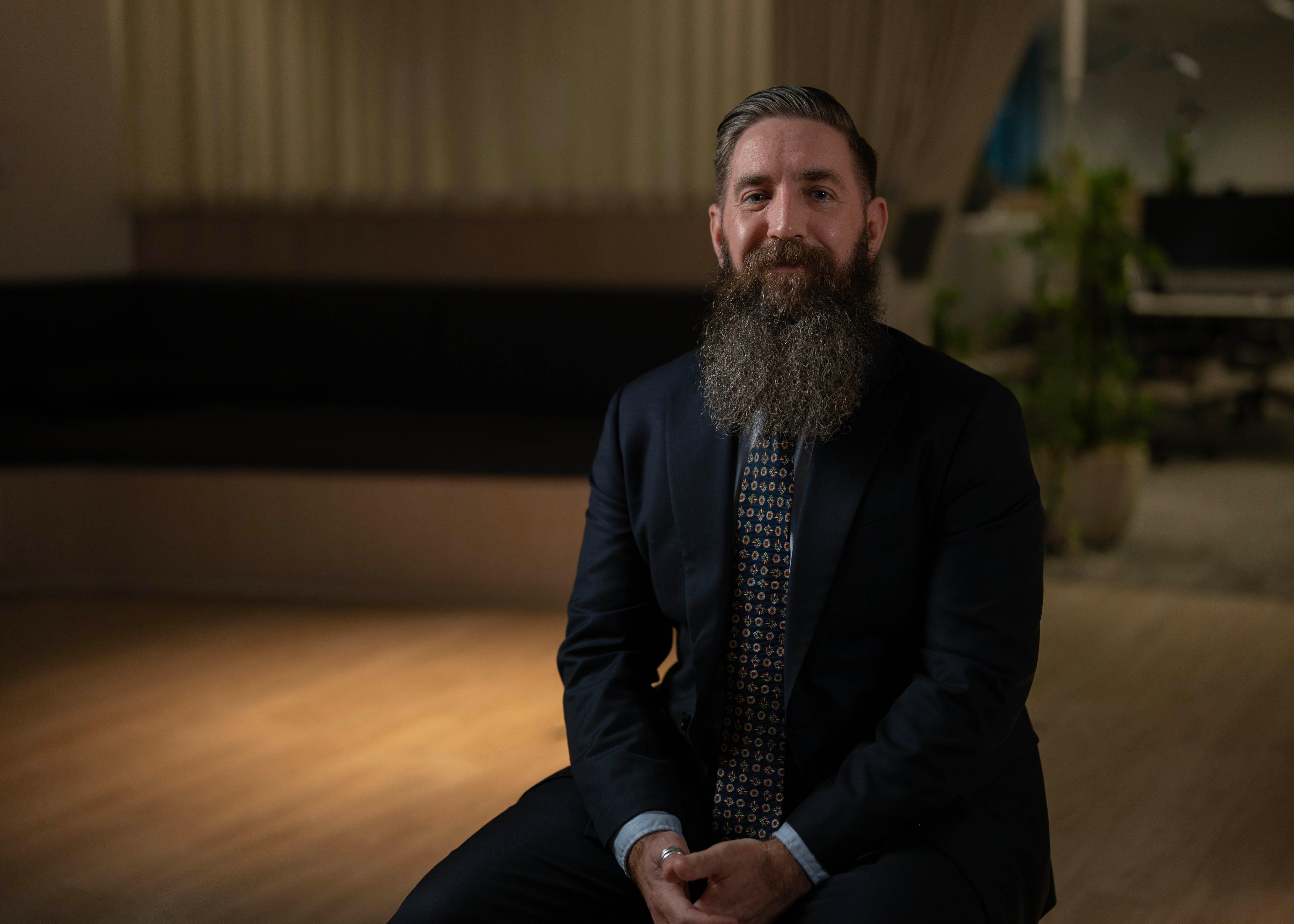 A man with a long beard sitting in a dark room. 