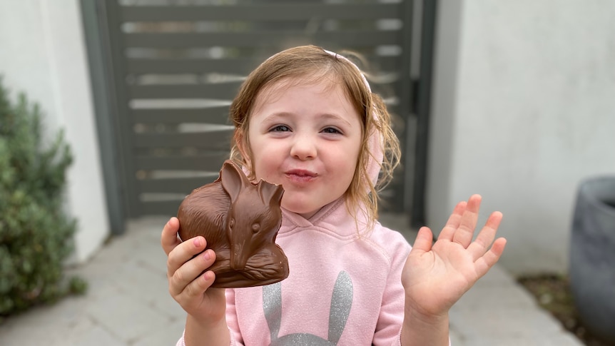 Young girl in pink jumper holding a chocolate bilby with one ear eaten
