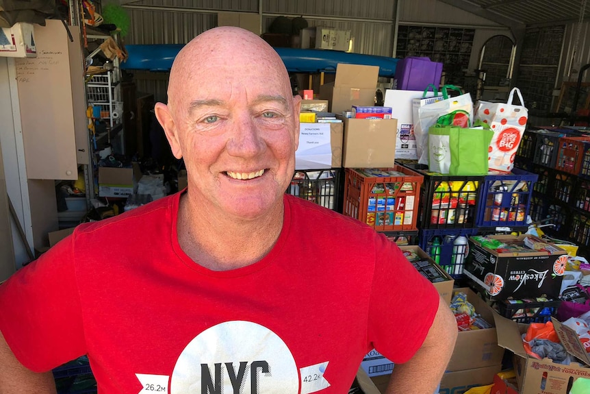 A man pictured in front of a shed filled with milk crates containing donated groceries.