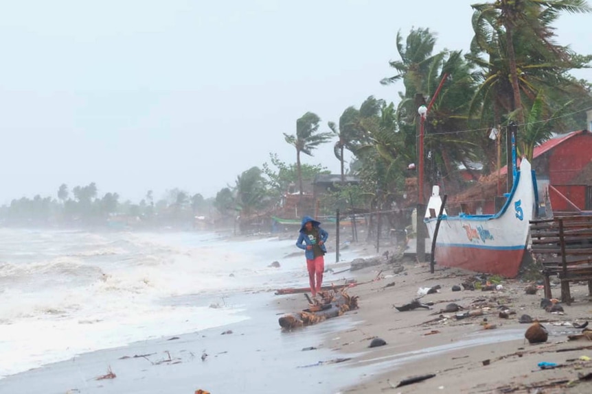 A person walks along a shoreline which is being battered by strong winds.