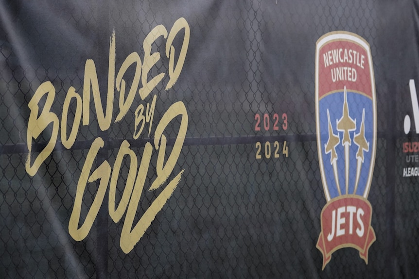 A banner with a Newcastle Jets logo on a gate at a sports field.