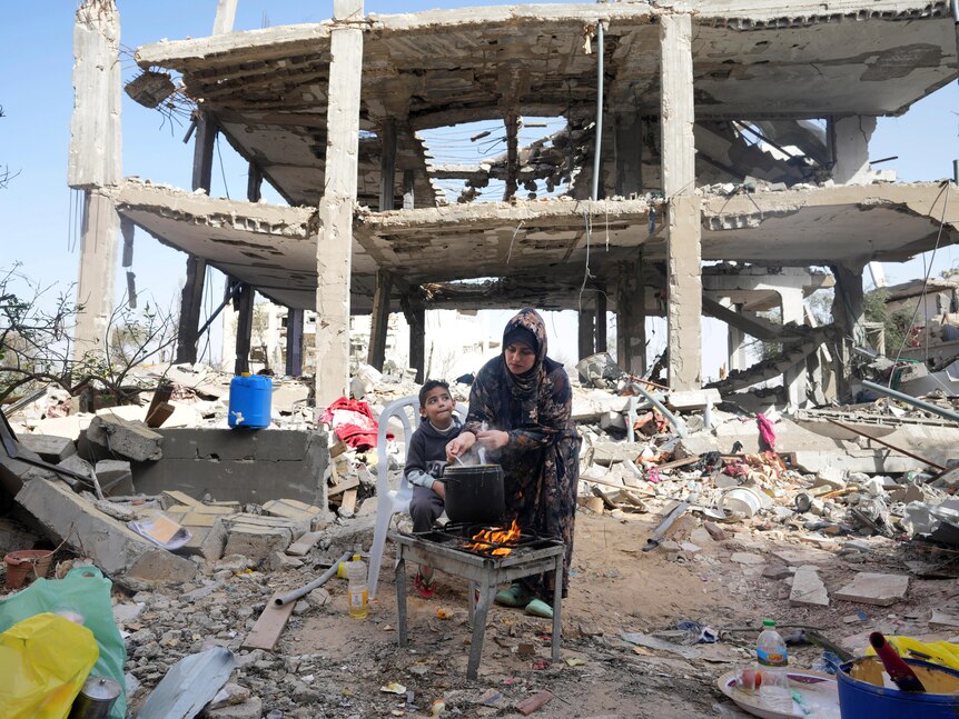 Palestinian woman cooks in front of her family's  building destroyed in the Israeli bombardment of Gaza