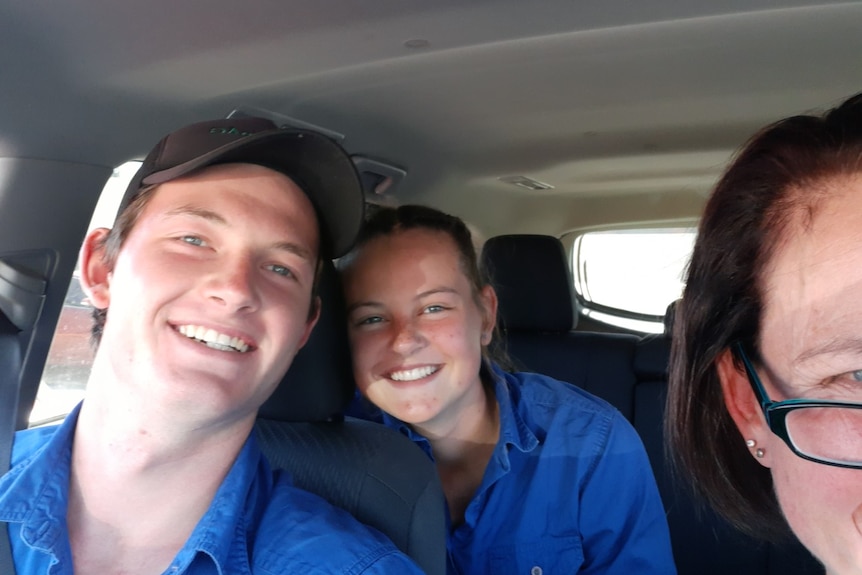 Two teenagers dressed in blue shirts smile while being passengers in a car.