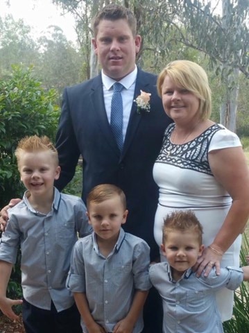 Family of mum, dad and three young boys standing outside all dressed up, smiling.