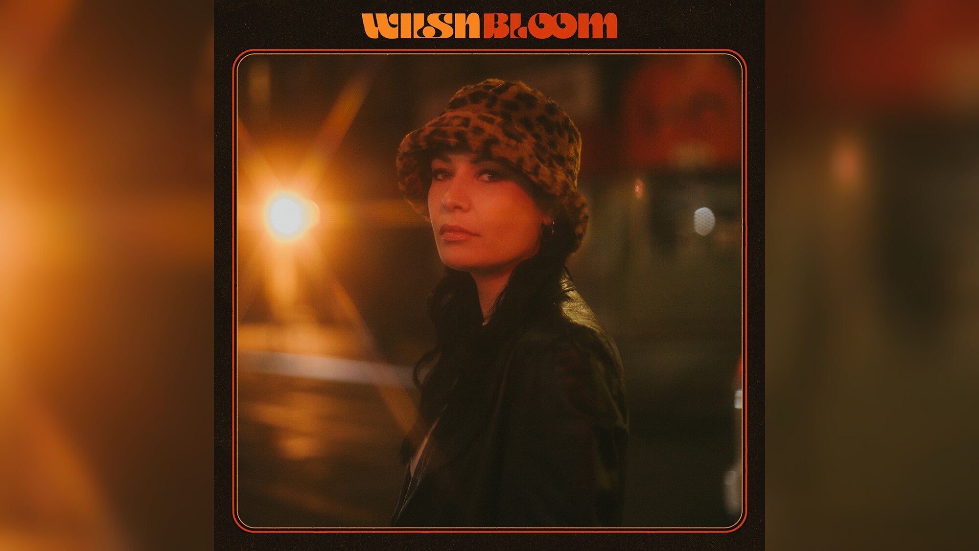 dark-haired woman with leopard print bucket hat and brown coat stands in street. Retro text reads: WILSN - Bloom