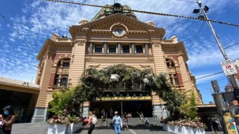 An archway of flowers stands outside Flinders Street Station on a sunny day.