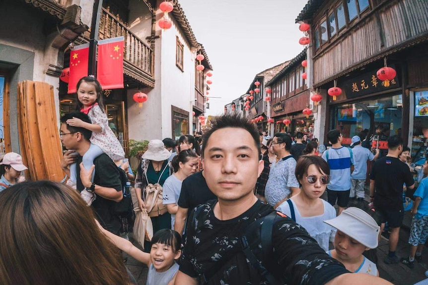 A man standing in the crowd and taking selfie.