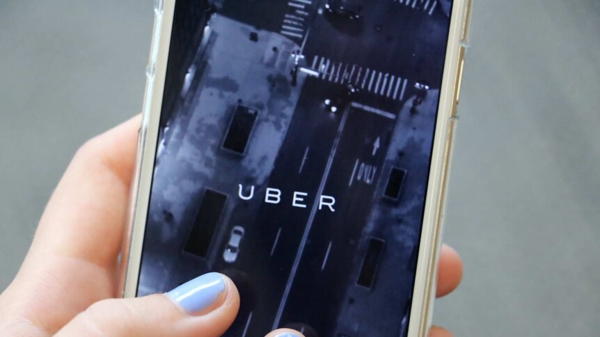 A woman holds a phone with the Uber app open.