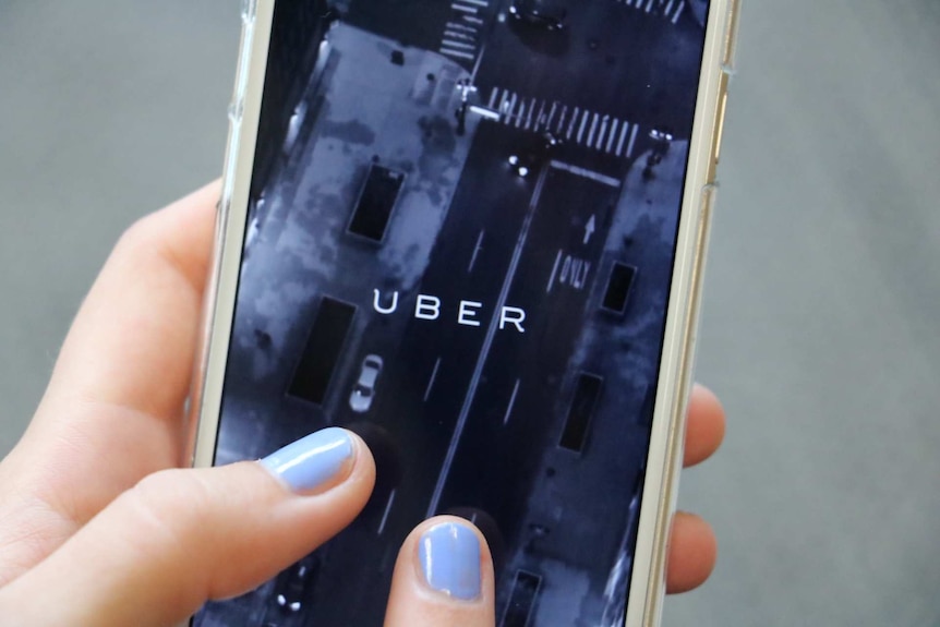 A person with painted nails operates the Uber app on a phone,