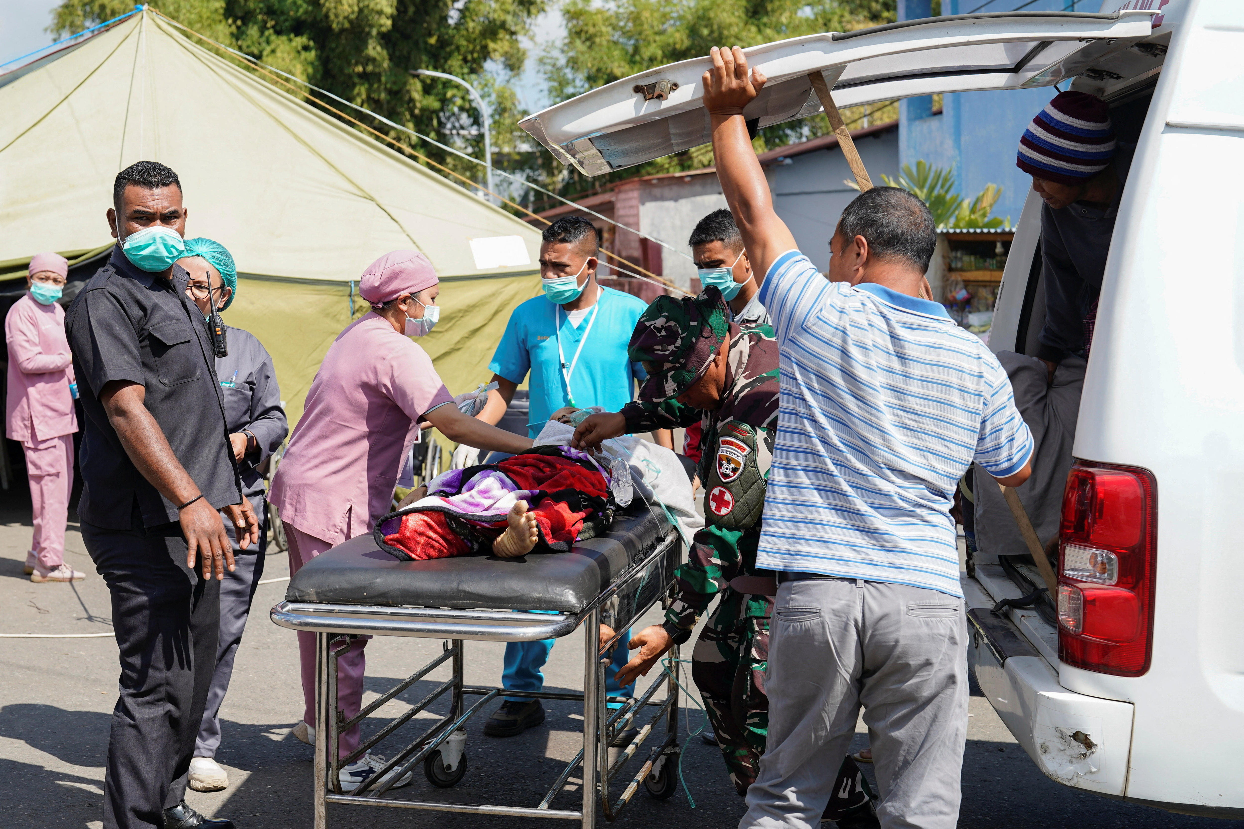 A group of health workers wearing masks tend to a person on a stretcher.