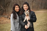 Two Latino women dressed in warm coats and a small dog pose for a photo.