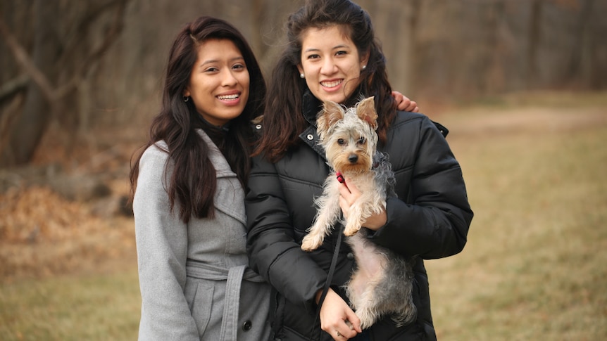 Two Latino women dressed in warm coats and a small dog pose for a photo.