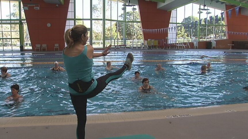 An aerobics instructor kicking her leg out to direct the class of women in an indoor pool.