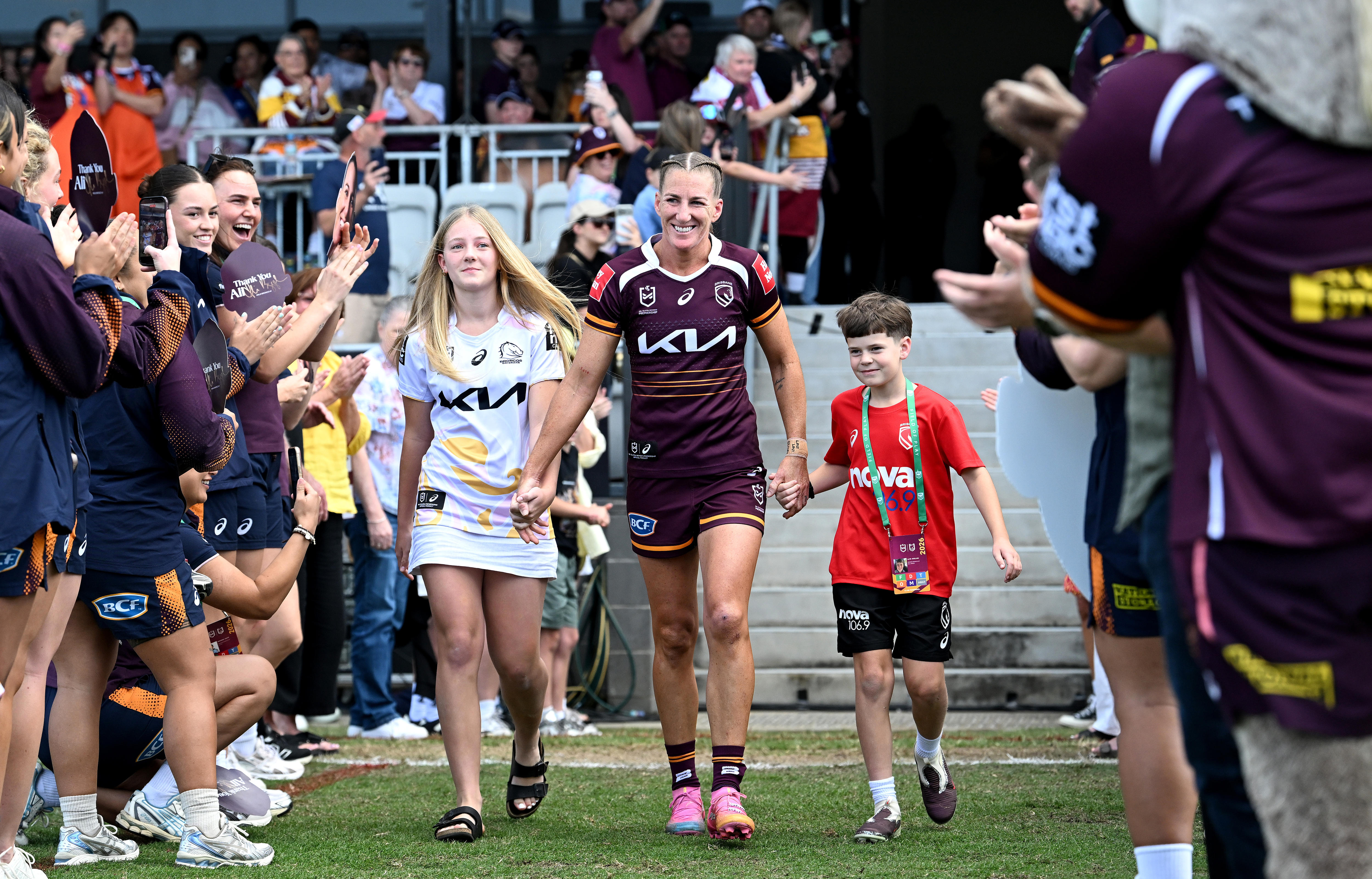 Ali Brigginshaw walks out, holding the hands of two children with players either side