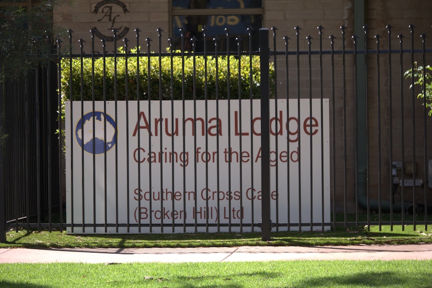 A sign at Aruma Lodge, with lawn and a footpath in front of the sign.