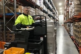 A man in  a high-vis vest on a forklift in a large warehouse.