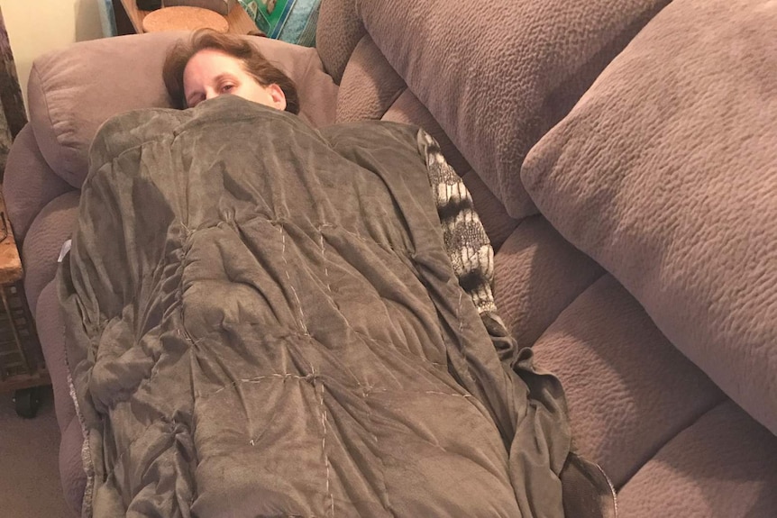 A woman covered by a weighted blanket on a couch