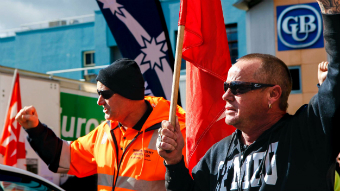 Two workers holding flags wave their arms in the air.