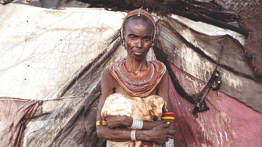 An elderly Rendille woman holds her newborn goat outside her house in northern Kenya.