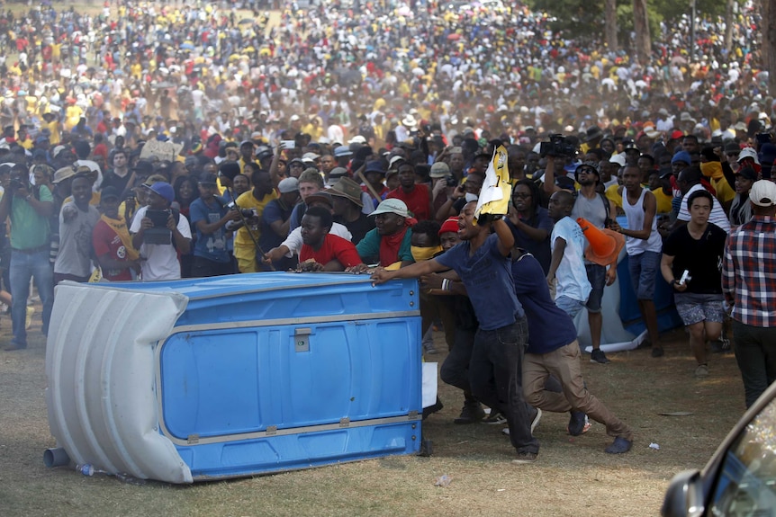 South African protesters push a portable loo before burning it