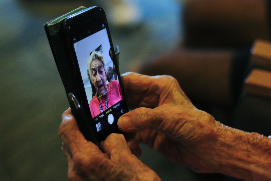 A photo of a phone being held in a elderly women's hands. On the screen is a photo of the woman's face in selfie mode.