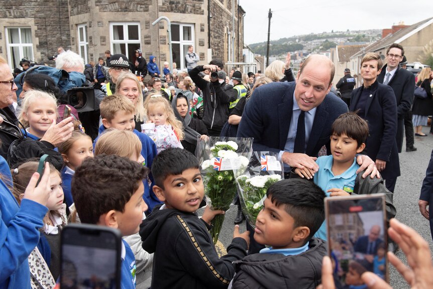 William leans down slightly to smile for a photo with a group of young boys waiting to meet him.
