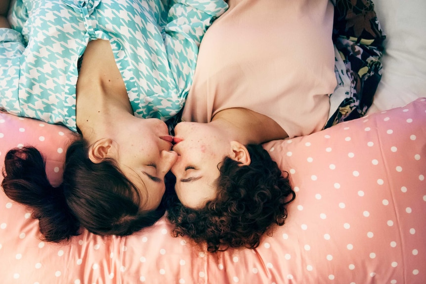 Two women lay in bed with lips touching for a story about asking for what you want in the bedroom during sex.