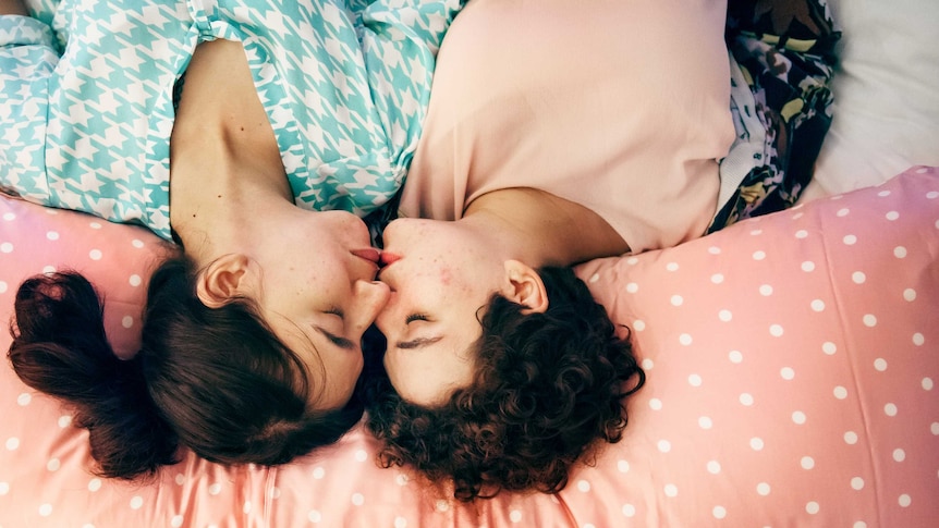 Two women lay in bed with lips touching for a story about asking for what you want in the bedroom during sex.