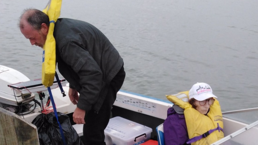 Felicity Loveday sits at the front of a boat while Adrian Meneveau stands at the stern. Both wear lifejackets.