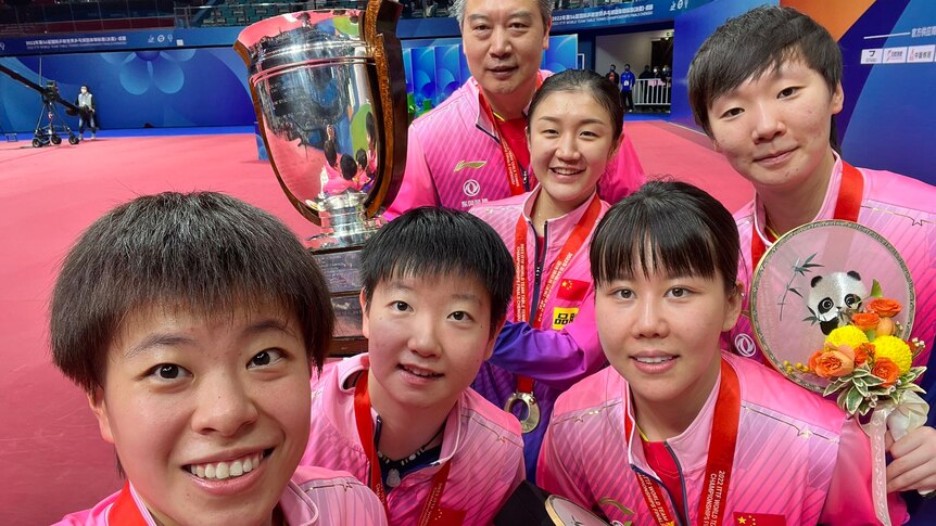 Five Chinese women and a man take a selfie with a large silver trophy