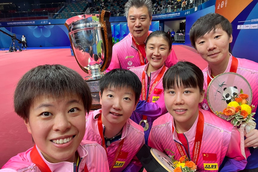 Five Chinese women and a man take a selfie with a large silver trophy