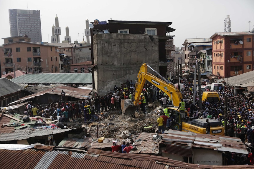 From an adjacent rooftop looking down, a vast crowd is packed into a tight Lagos city block with rubble in the centre of it.