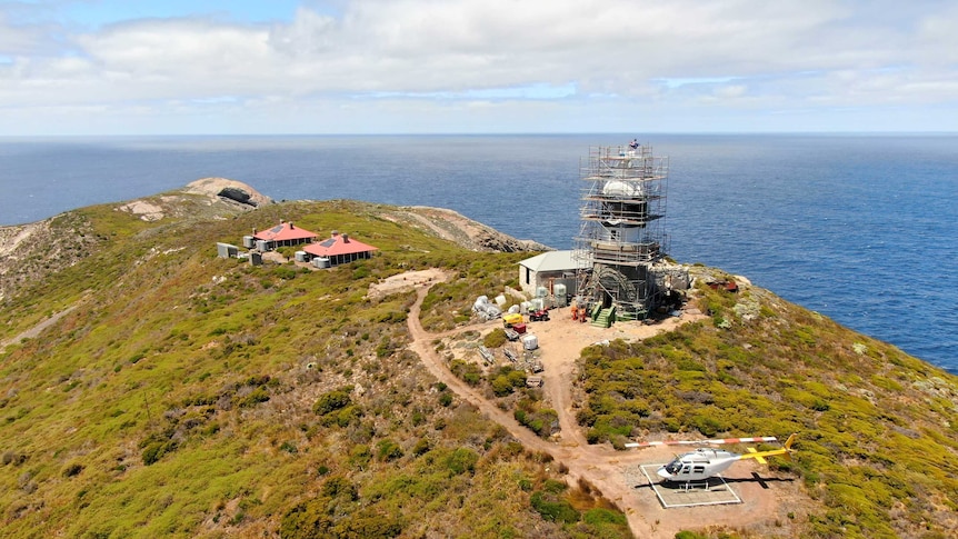 A drone shot of a lighthouse on an island out to sea.