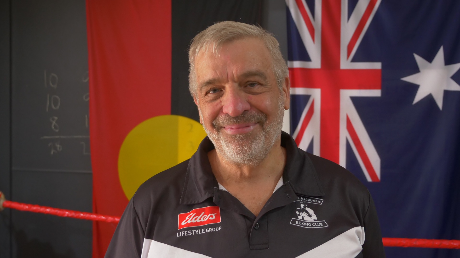 Homem sorrindo em frente às bandeiras aborígenes e australianas