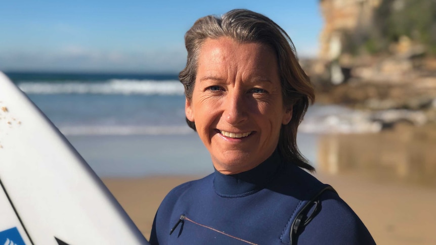 Layne Beachley holds a surfboard on a beach