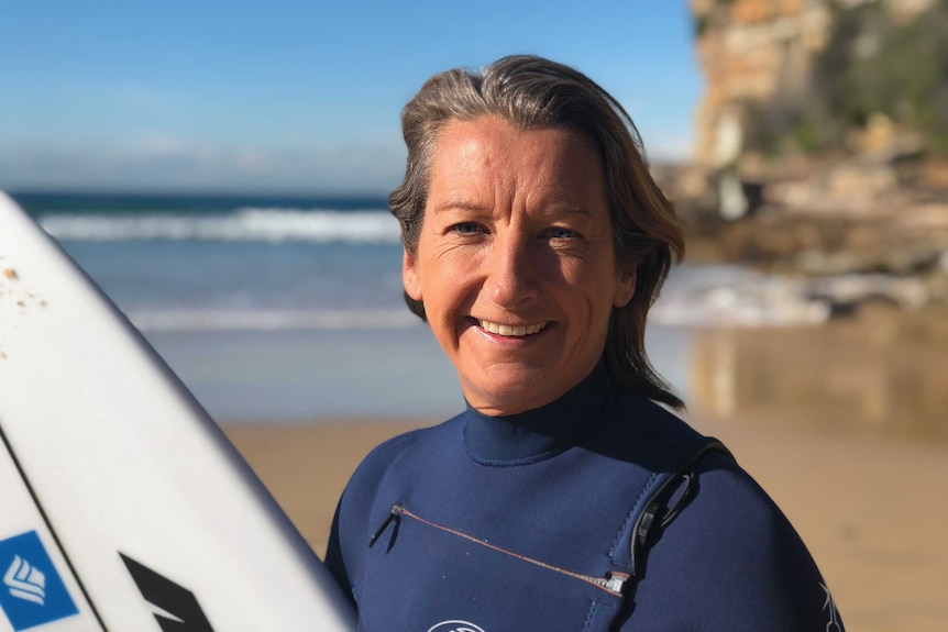 Layne Beachley holds a surfboard on a beach