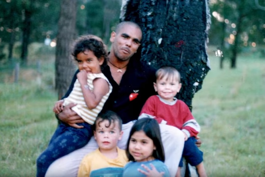 Blurry family photo of Indigenous man with four children sitting under a tree.