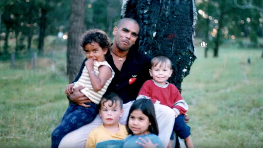 Blurry family photo of Indigenous man with four children sitting under a tree.