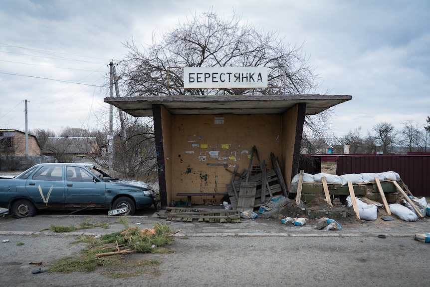 A car marked with a "V" by Russian troops sits next to a sandbagged bus stop in Borodyanka