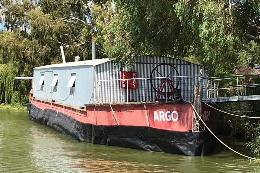 An old barge with a corrugated iron pump shed is floating on the river.