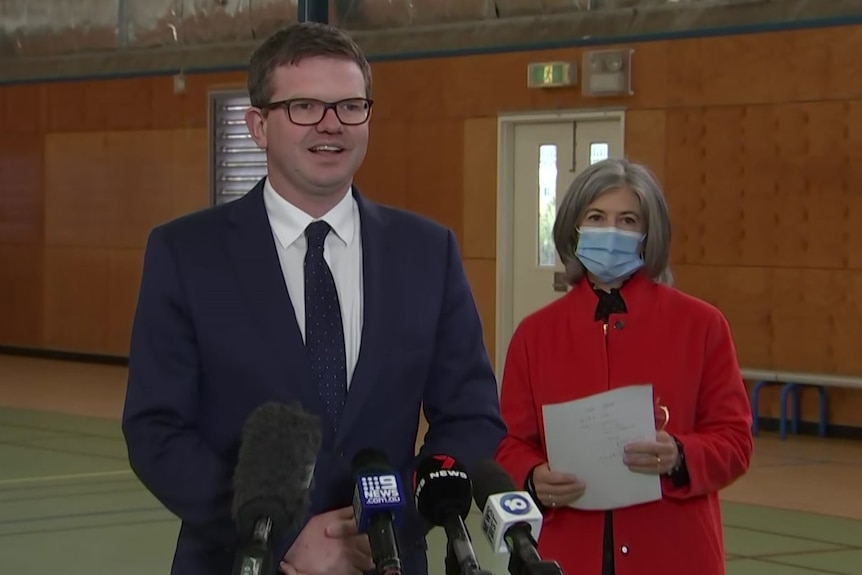 Two men wearing suits and a woman wearing a red coat inside a school gym