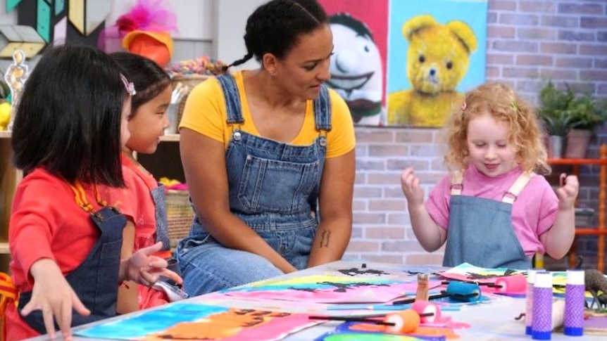 Zindzi sitting at a desk with children looking at their artwork
