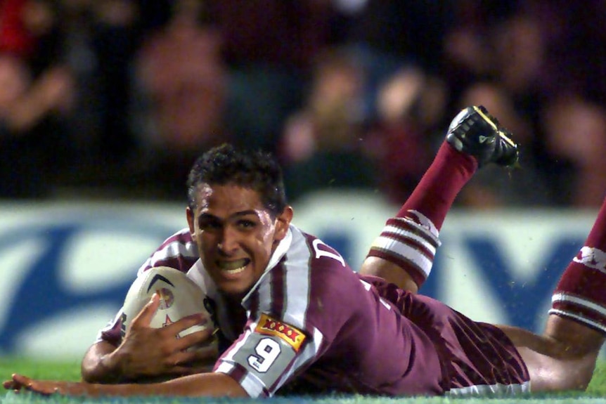 A man scoring a try in rugby league, he is laying on the grass holding the rugby ball